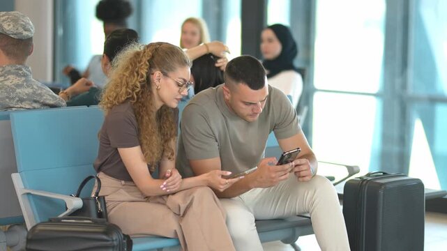 Young couple using smartphones while waiting for their flight at the airport