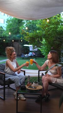 Smiling female friends talking and toasting with juice at a garden cafe