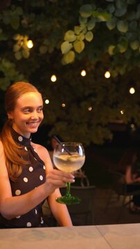 Young woman enjoying a cocktail at an outdoor restaurant at night