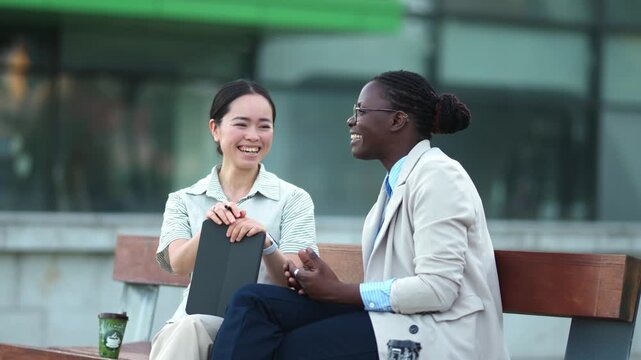 Multiracial businesswomen laughing together on a bench outdoors