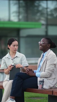 Two diverse businesswomen discussing a project on a park bench