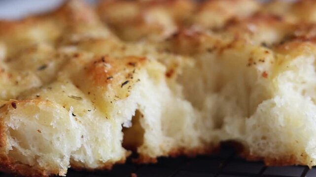 Macro shot panning across the golden crust of freshly baked Italian focaccia bread topped with herbs, salt, and spices. Detailed view of the textured surface showing rosemary, pepper, and seasonings o