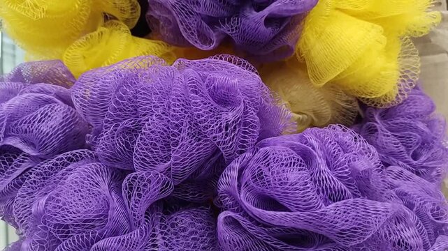 Close-up of colorful plastic mesh bath sponges and loofahs in purple, yellow, and orange. Ideal for hygiene, shower, and bathroom concepts.