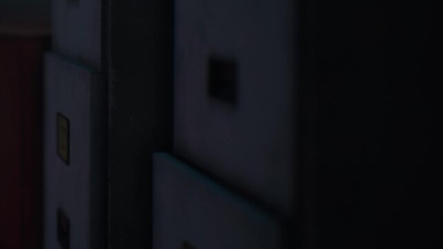 A view shows several storage boxes lined up against a wall in a dark room. The low light creates shadows and highlights the corners of the boxes, hinting at their contents.