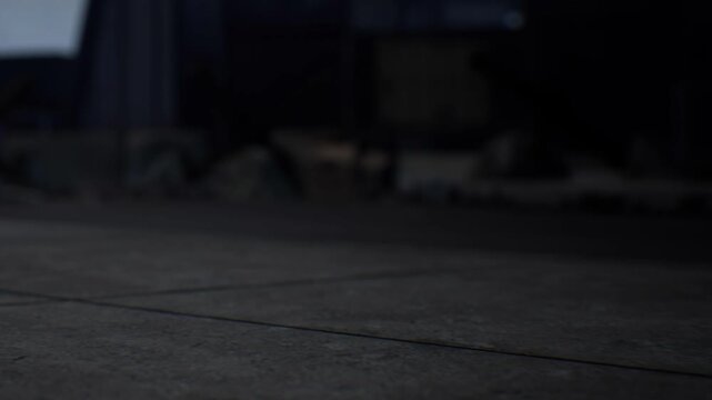 The scene shows a concrete floor with various objects scattered around. Shadows create a soft focus effect. It is a low light environment, adding a sense of depth and dimension.