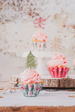 Close-up of three vanilla sponge Cupcakes with pink buttercream icing decorated with Christmas trees on a table