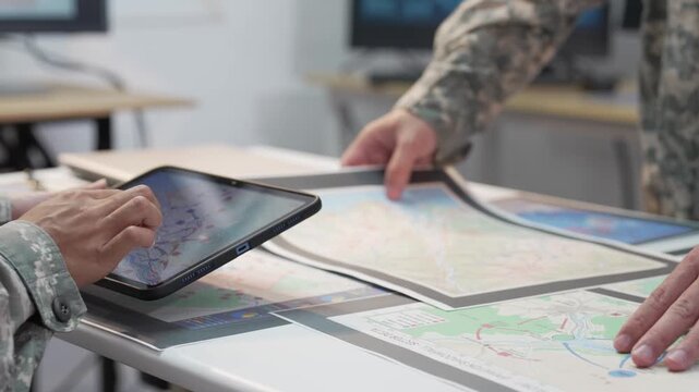 Military officers analyzing tactical map documents and digital tablet in command war room