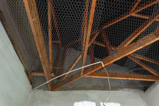 Attic ceiling showing wooden trusses and wire mesh safety net