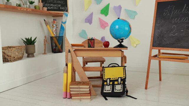 Empty primary interior school classroom setup with wooden desk, globe, apple, chalk board easel. Back to school concept, colorful paper airplanes wall decor, study background, and school supplies.