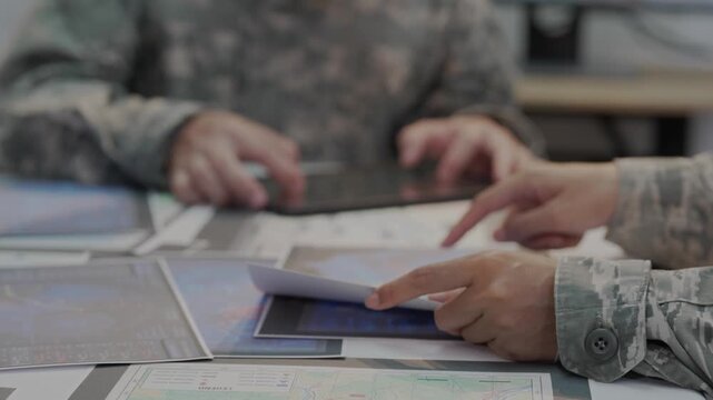 Military officers analyzing tactical map documents and digital tablet in command war room
