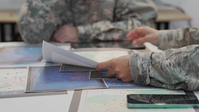 Military officers analyzing tactical map documents and digital tablet in command war room