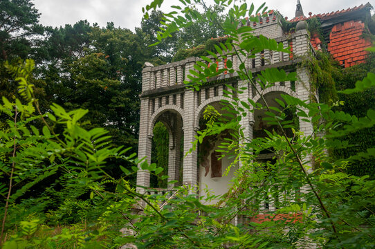 Abandoned overgrown mansion with spiral staircase, old car and ruined interior