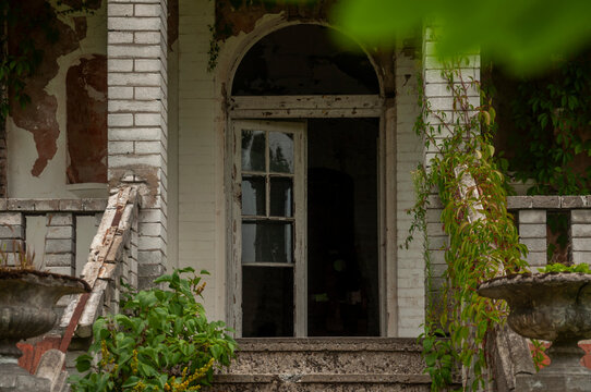 Abandoned overgrown mansion with spiral staircase, old car and ruined interior
