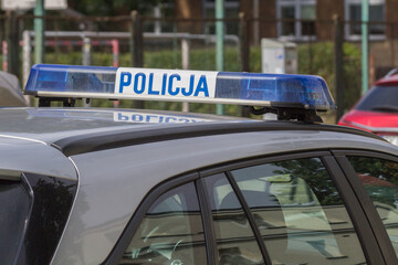 Niebieska belka sygnalizacyjna z napisem Policja na dachu radiowozu.