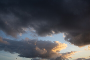 Obraz premium Dramatic Storm Clouds at Sunset with Golden Light on the Horizon. Dramatic evening sky photographed shortly before a storm, with massive dark clouds spreading across the horizon and warm golden sunlig
