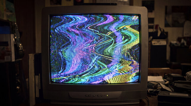 Old CRT television with colorful VHS glitch and psychedelic static on screen. Retro analog TV noise with wavy distortion in purple, blue, green and yellow.

