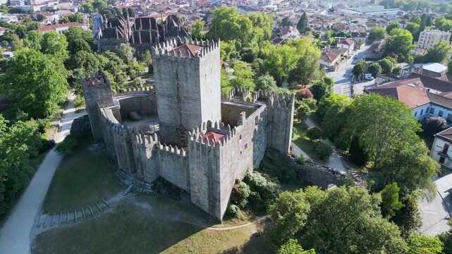 Majestic aerial view of the medieval Guimaraes Castle, a significant landmark in Portugal, surrounded by lush green trees and the city