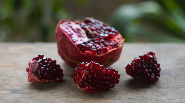 Ripe opened pomegranate fruit with seeds on dark wooden table.