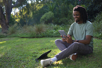 African American man sitting on grassy lawn holding tablet, black bag with cable, copy space © WavebreakMediaMicro