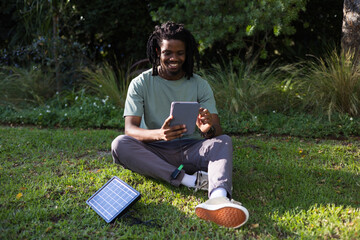 Adult African man sitting cross-legged on grassy lawn in park using tablet with solar battery pack © WavebreakMediaMicro