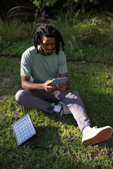 African American man sitting on lawn wearing light-green shirt using tablet with solar panel © WavebreakMediaMicro