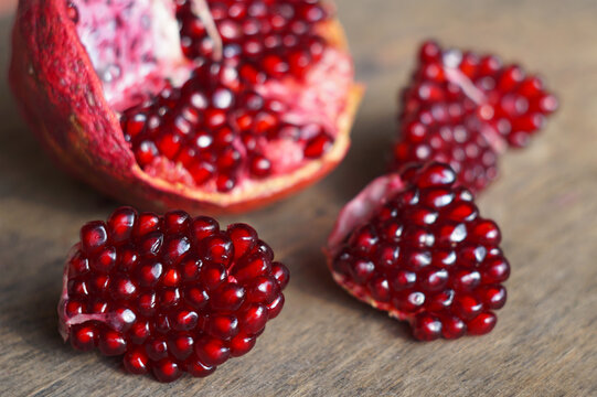 Selective focus on fresh pomegranate chunks with ruby red seeds on wooden surface.