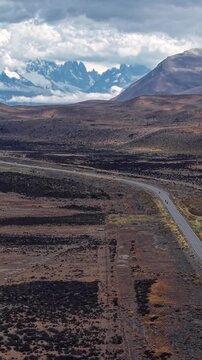 Aerial view of a scenic road winding through the arid landscape of Patagonia, Argentina, with snow-capped mountains in the background