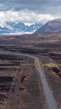 Aerial view of a road stretching through the vast arid landscape of Patagonia, Argentina, with snow-capped mountains in the distance