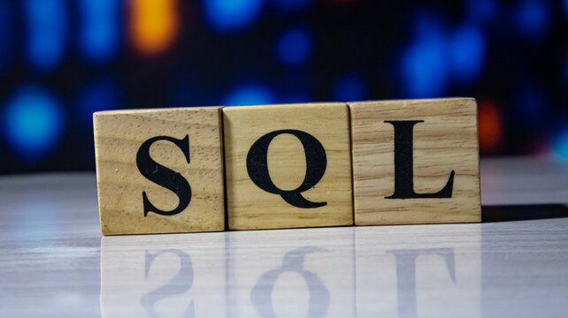 SQL letters printed on wooden cubes arranged in a line with blue bokeh background.