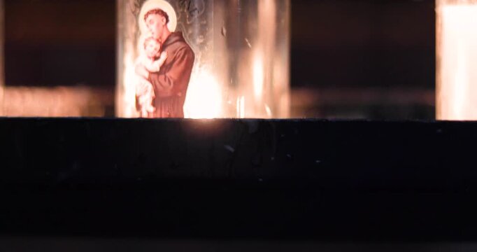 A luminous candle with Saint Anthony of Padua and the Christ Child in a church.