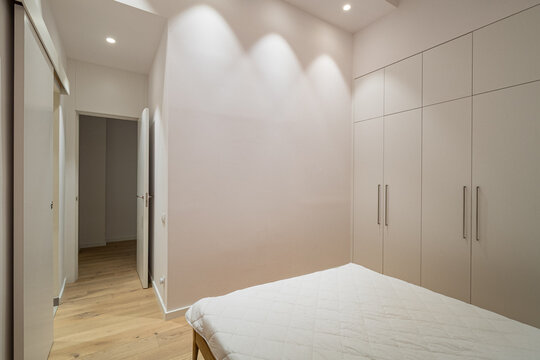 Minimalist modern bedroom with white bed, light wood flooring, builtin wardrobes, and soft recessed lighting in calm contemporary residential interior, with bedroom, minimalist, modern, white detail