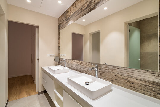 Modern bathroom interior with double countertop sinks wooden accent and large mirror under bright recessed lighting