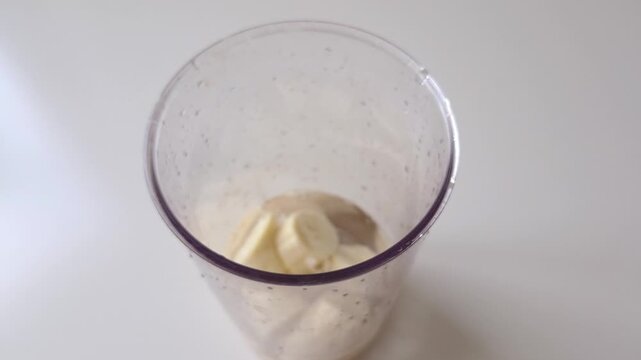 Pouring fresh water into blender cup with sliced bananas for healthy smoothie cooking