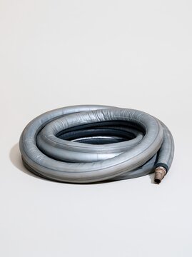 Coiled rubber inner tube with a vulcanized repair patch, featuring a worn matte finish and scuffed valve on a white background with copy space