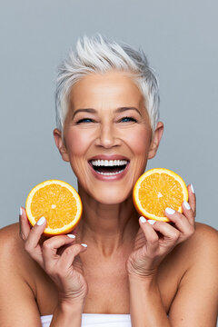 Elderly woman with short white hair holding two orange slices.