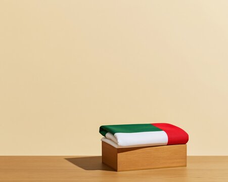 UAE flag folded in a wooden box on a timber table, featuring soft fabric textures and hard side lighting with copy space for heritage layouts