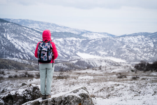 Back view of a woman with a backpack, admiring a vast snow-covered mountain landscape during a winter hike. Long shot.