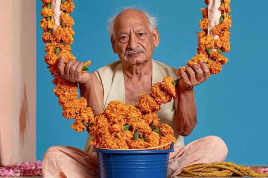 Senior man gathering wilted marigold flowers into a blue bucket on a wet stone doorstep for waste and reuse
