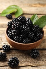 Ripe blackberries in bowl with leaves on wooden table, closeup © New Africa
