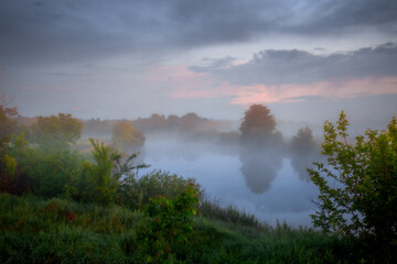 Morning fog drifting over a calm river surrounded by summer greenery © Yaroslav