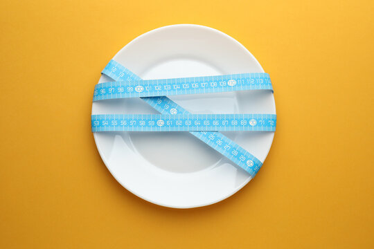 Anorexia. Plate with measuring tape on orange background, top view
