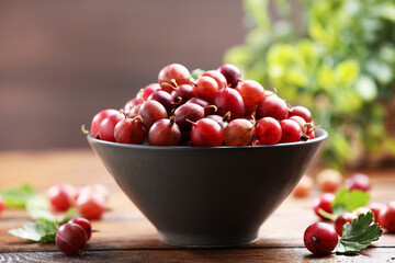 Fresh red gooseberries in bowl and green leaves on wooden table, closeup © New Africa