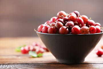 Fresh red gooseberries in bowl on wooden table, closeup. Space for text © New Africa