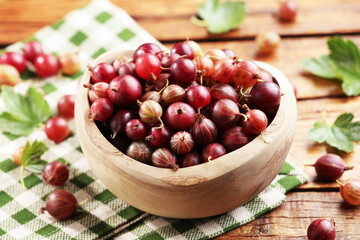 Fresh red gooseberries in bowl and green leaves on wooden table, closeup © New Africa