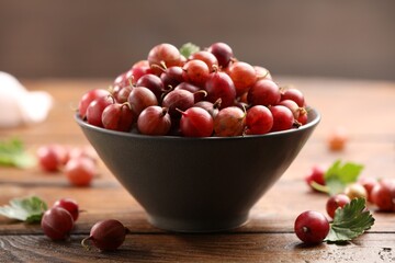 Fresh red gooseberries in bowl and green leaves on wooden table, closeup © New Africa