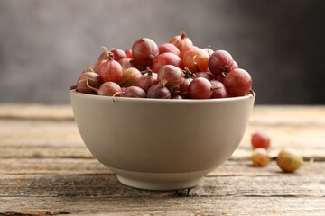Fresh red gooseberries in bowl on wooden table, closeup © New Africa