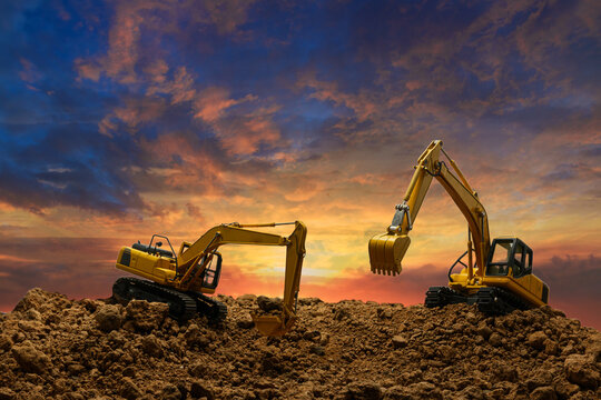 Two Crawler excavators  are digging the soil in the construction site on   sunset clouds  sky background .