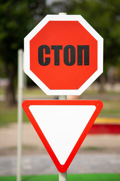 Stop sign in Ukrainian STOP with a yield sign mounted below it on a post against an outdoor background.