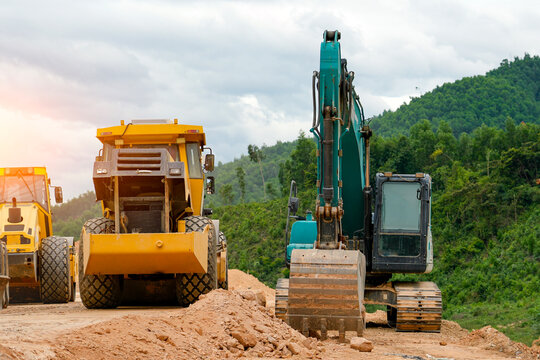 Heavy equipment, vibratory rollers and an excavator, are used to construct a highway among mountains and hills.
