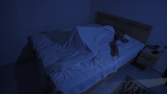 Man unable to sleep in hot bedroom, tossing and turning and throwing off sheet from heat at night with air conditioner
